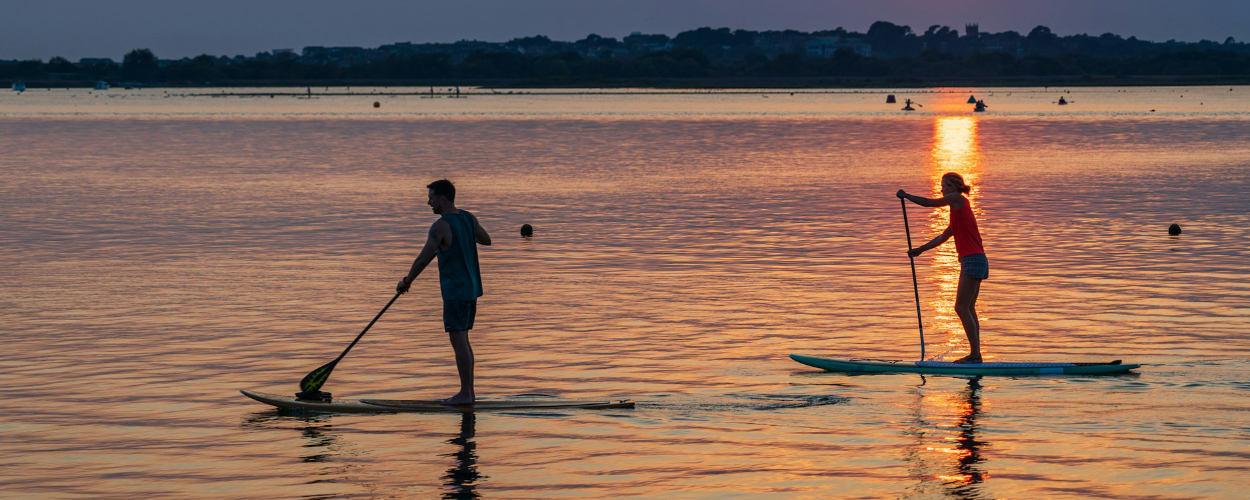 Deux personnes en paddle sur une eau calme au coucher du soleil, illustrant le retour progressif à la fluidité et à la disponibilité des ressources.