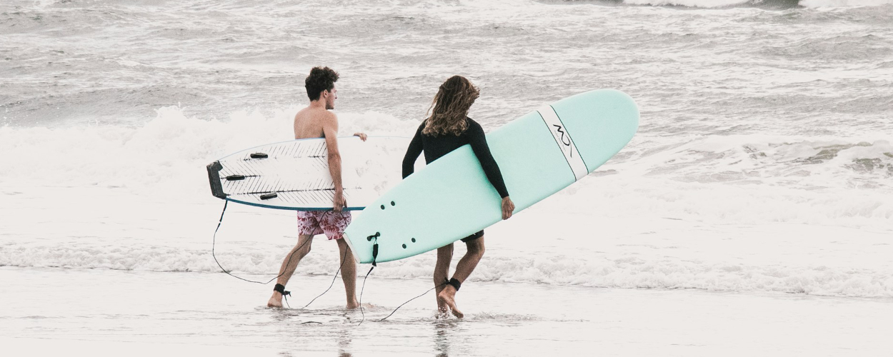 Deux personnes marchent vers l'océan avec leurs planches de surf, illustrant le retour de la disponibilité mentale et du réengagement.