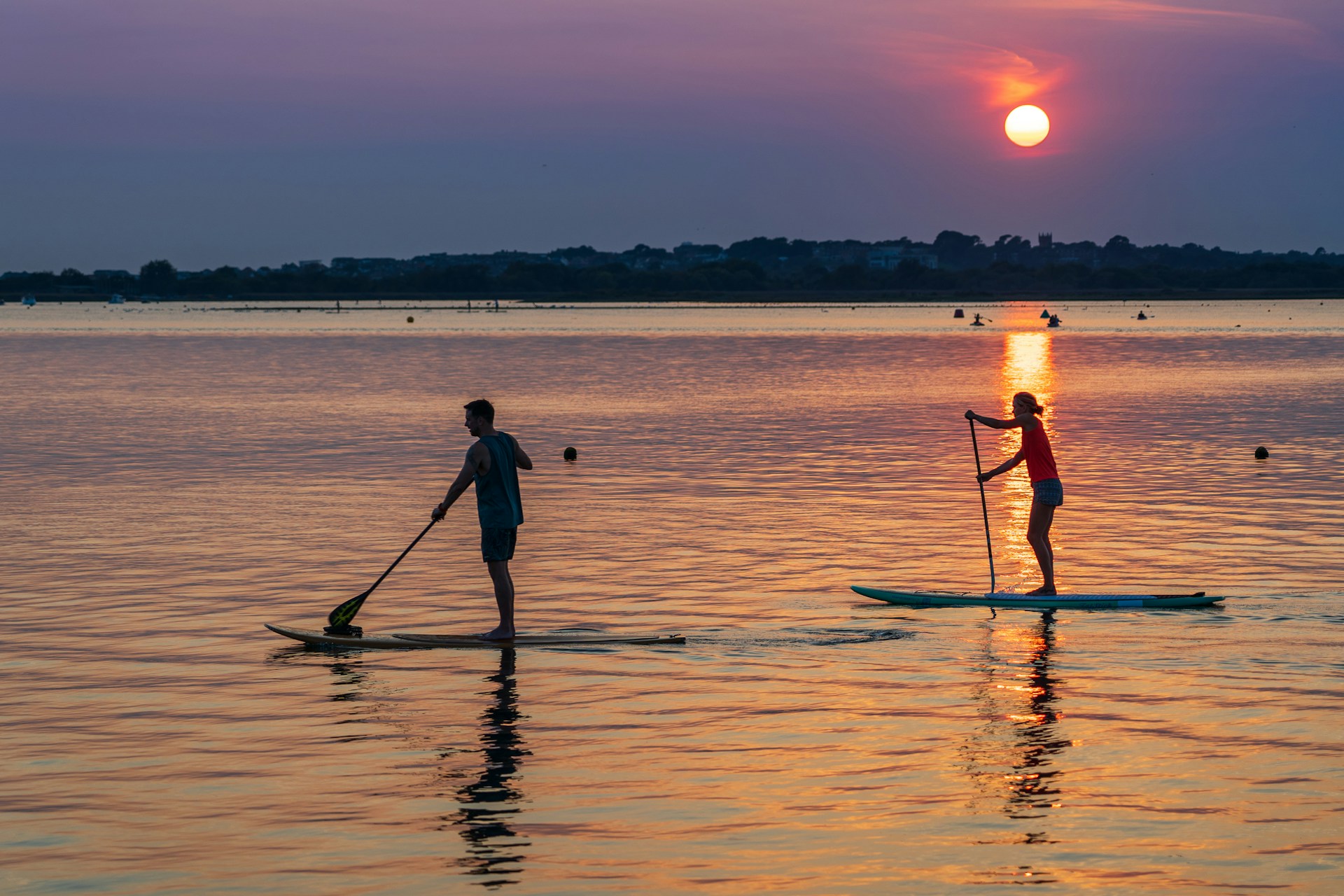 Deux personnes avancent en paddle sur une eau calme au coucher du soleil. L'image illustre la capacité à observer, s'ajuster et s'adapter aux variations de l'environnement pour maintenir l'équilibre et poursuivre sa progression.
